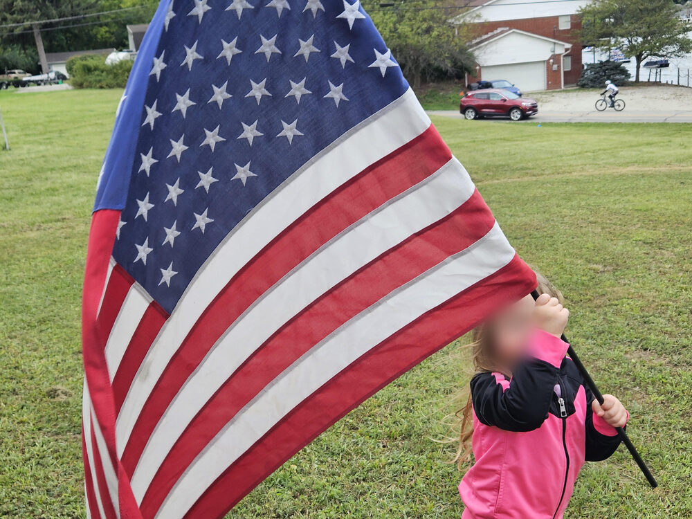 A child holding a large American flag on a lawn.